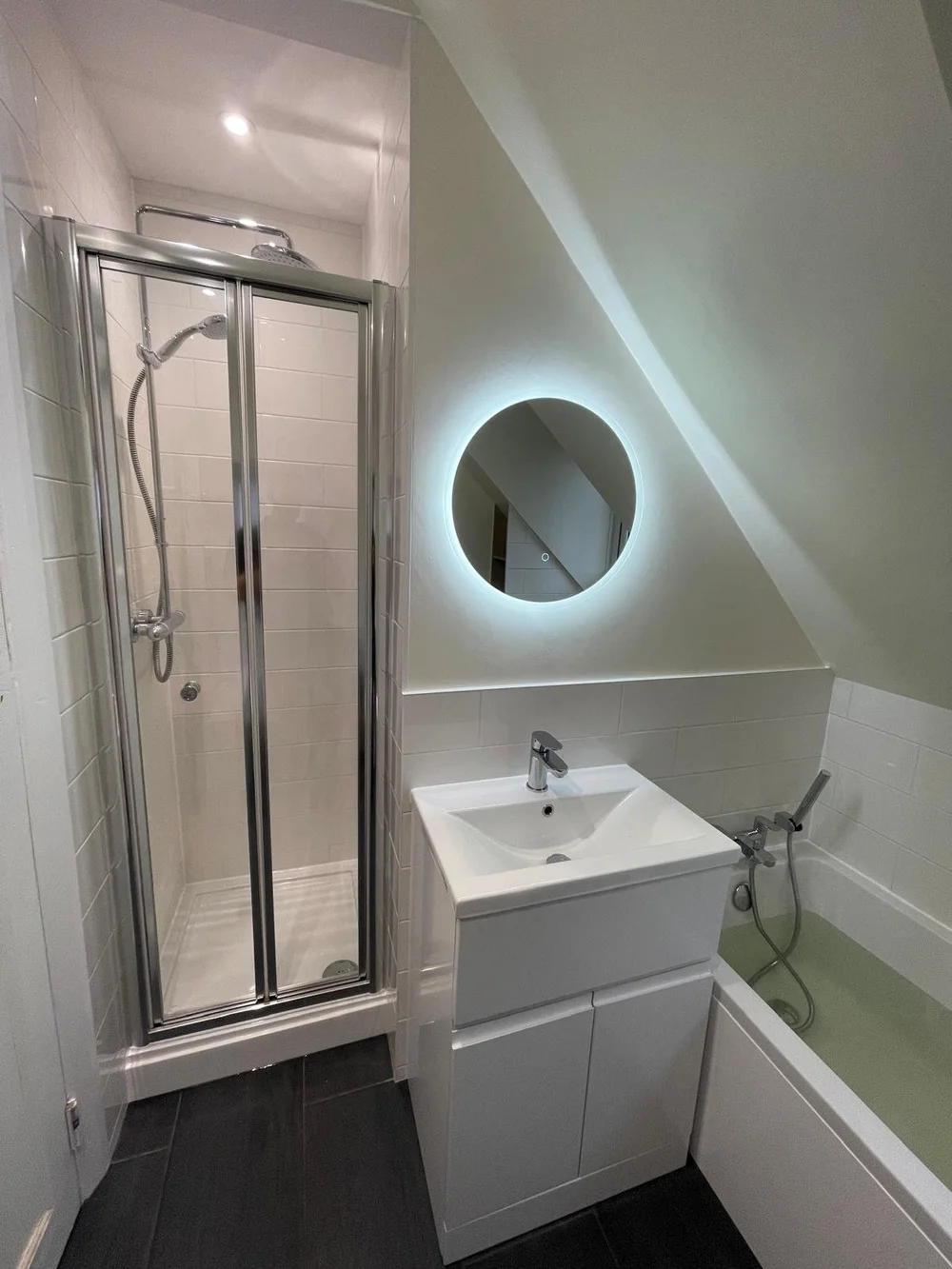 Compact loft shower room with backlit round mirror and bi-fold shower door — bathroom renovation Godalming