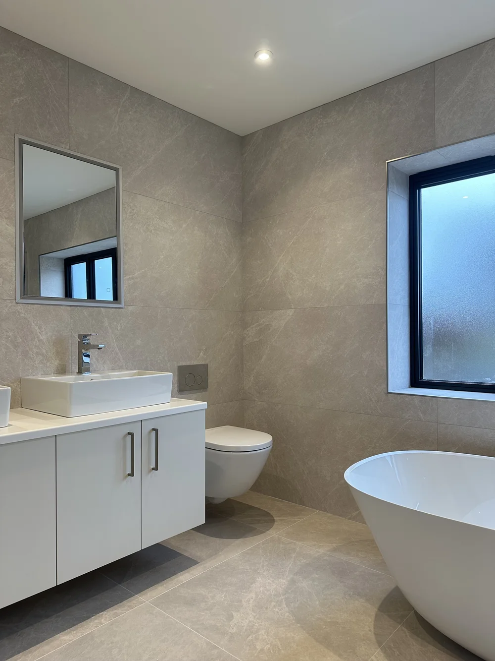 Contemporary stone-tiled bathroom with freestanding bath, floating vanity and twin basins — bathroom renovation Godalming