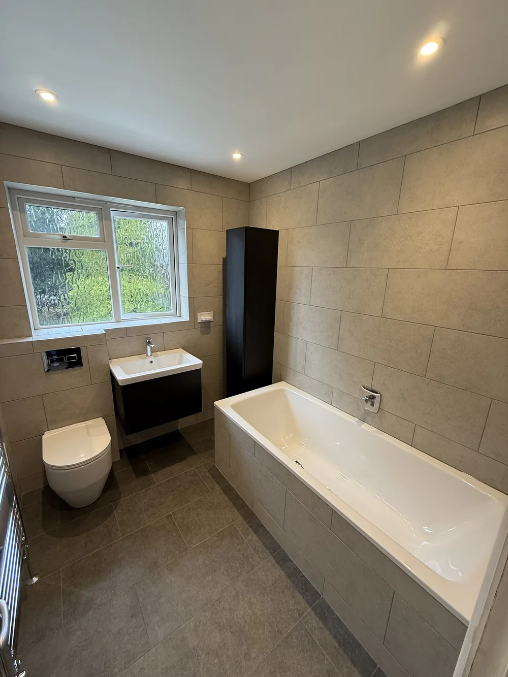 Fitted family bathroom with black vanity, tall storage and built-in bath — bathroom installers Godalming