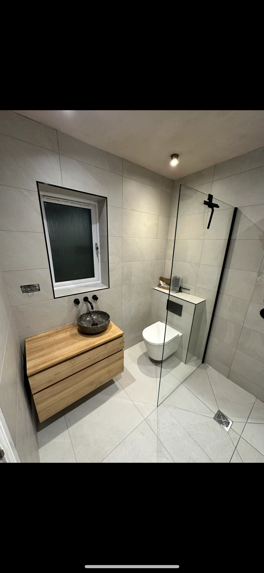 Wet room with oak floating vanity, stone vessel basin and black-framed walk-in shower — wet room installation Godalming