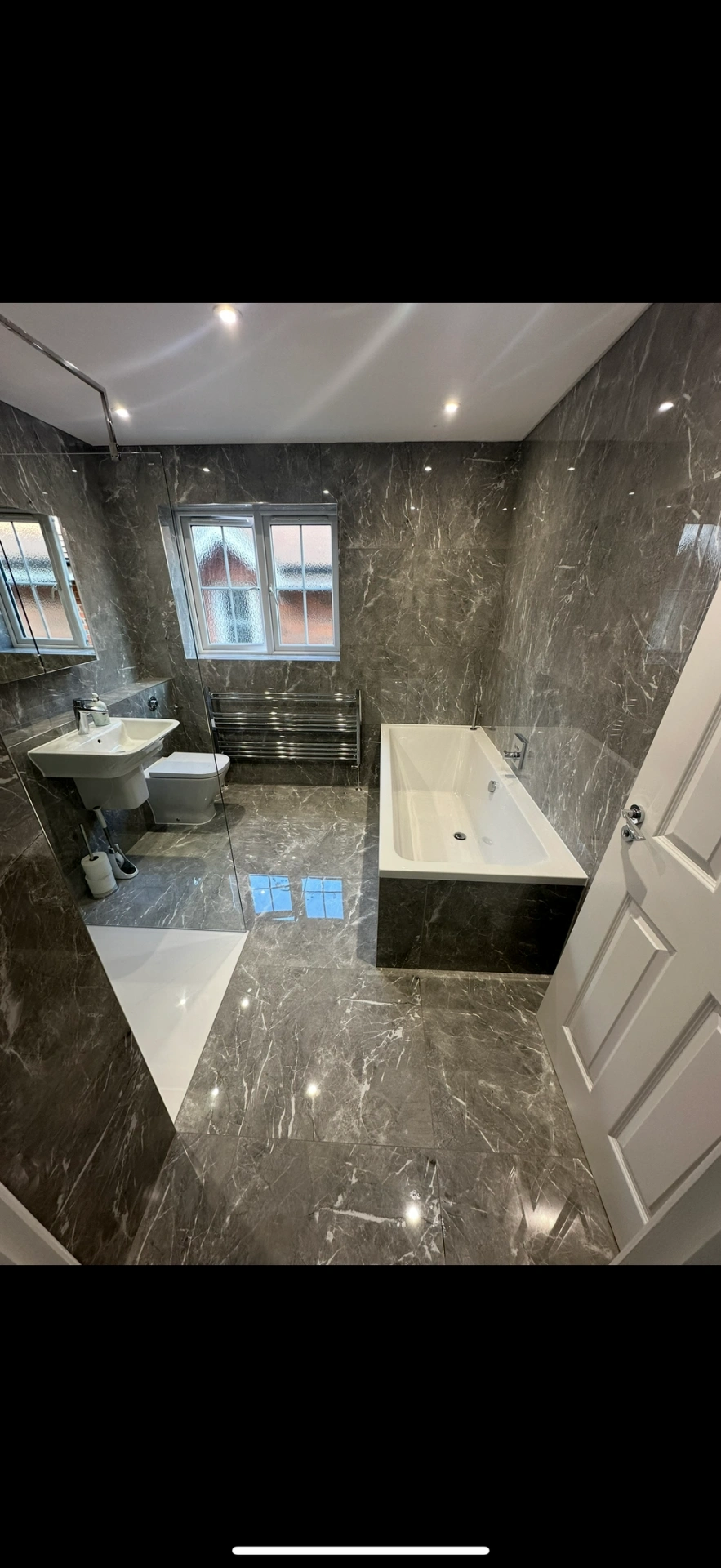 Grey marble family bathroom with double-ended bath and chrome towel rail — Godalming