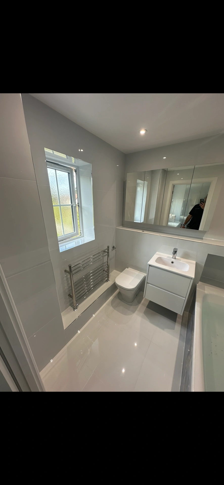 Bright white family bathroom with floating vanity, mirrored cabinet and gloss floor tiles — bathroom installation Godalming