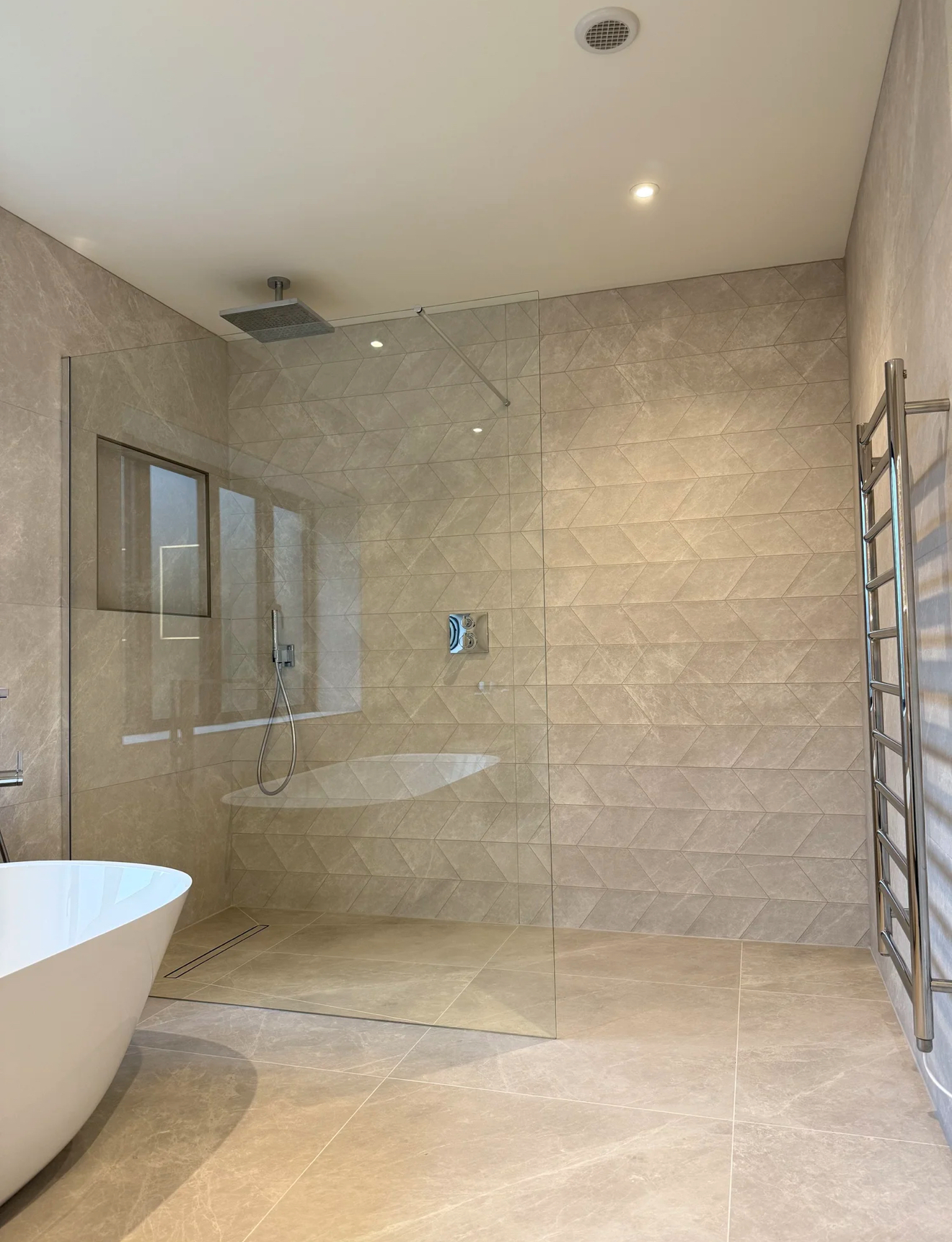 Beige marble wet room with freestanding bath, rainfall shower and chevron tiling — recent bathroom project Godalming