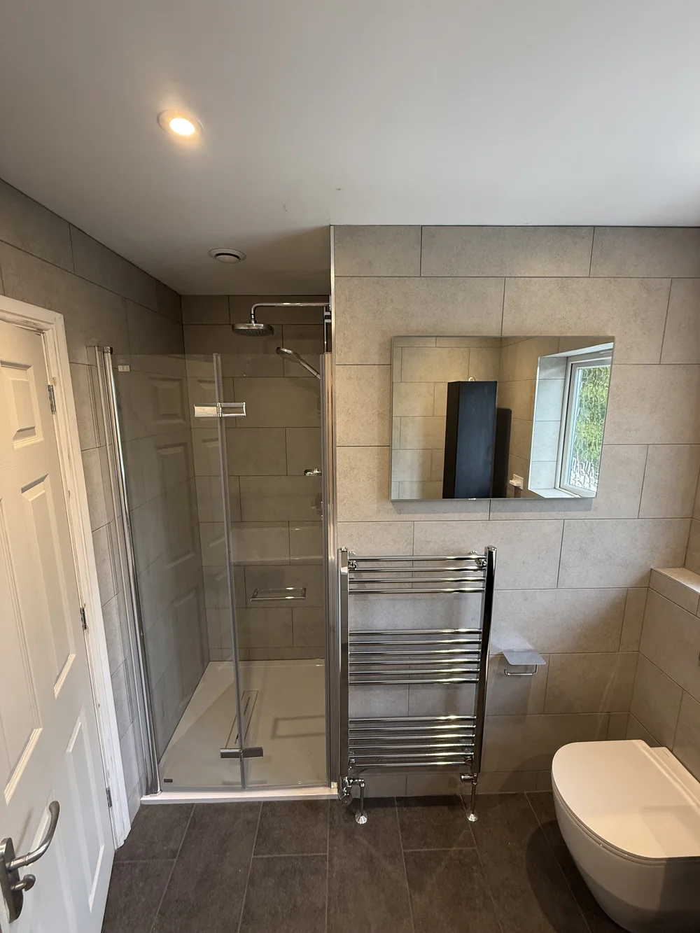 Stone-tiled family bathroom with hinged glass shower enclosure and chrome towel rail — bathroom installation Godalming