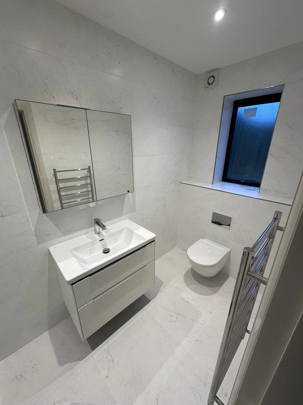White marble ensuite with wall-hung vanity, mirrored cabinet and back-to-wall WC — Godalming