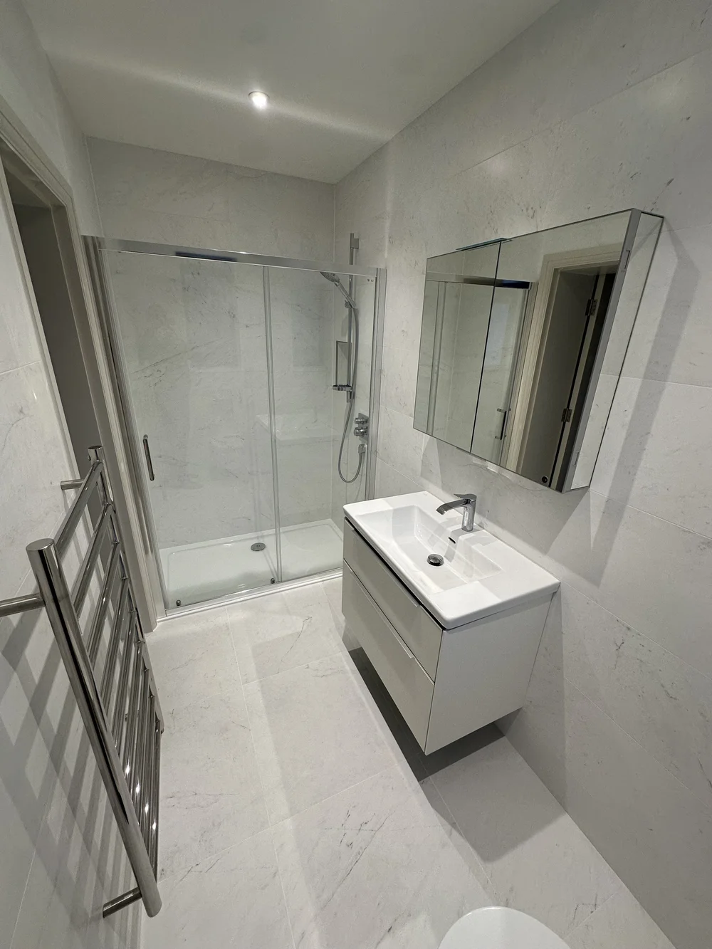 White marble shower room with sliding enclosure, wall-hung vanity and heated ladder rail — bathroom installation Godalming
