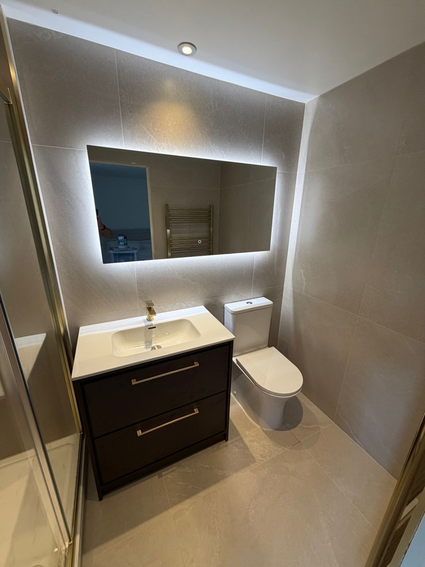 Beige ensuite with backlit LED mirror, dark wood vanity and brass fittings — recent project Godalming