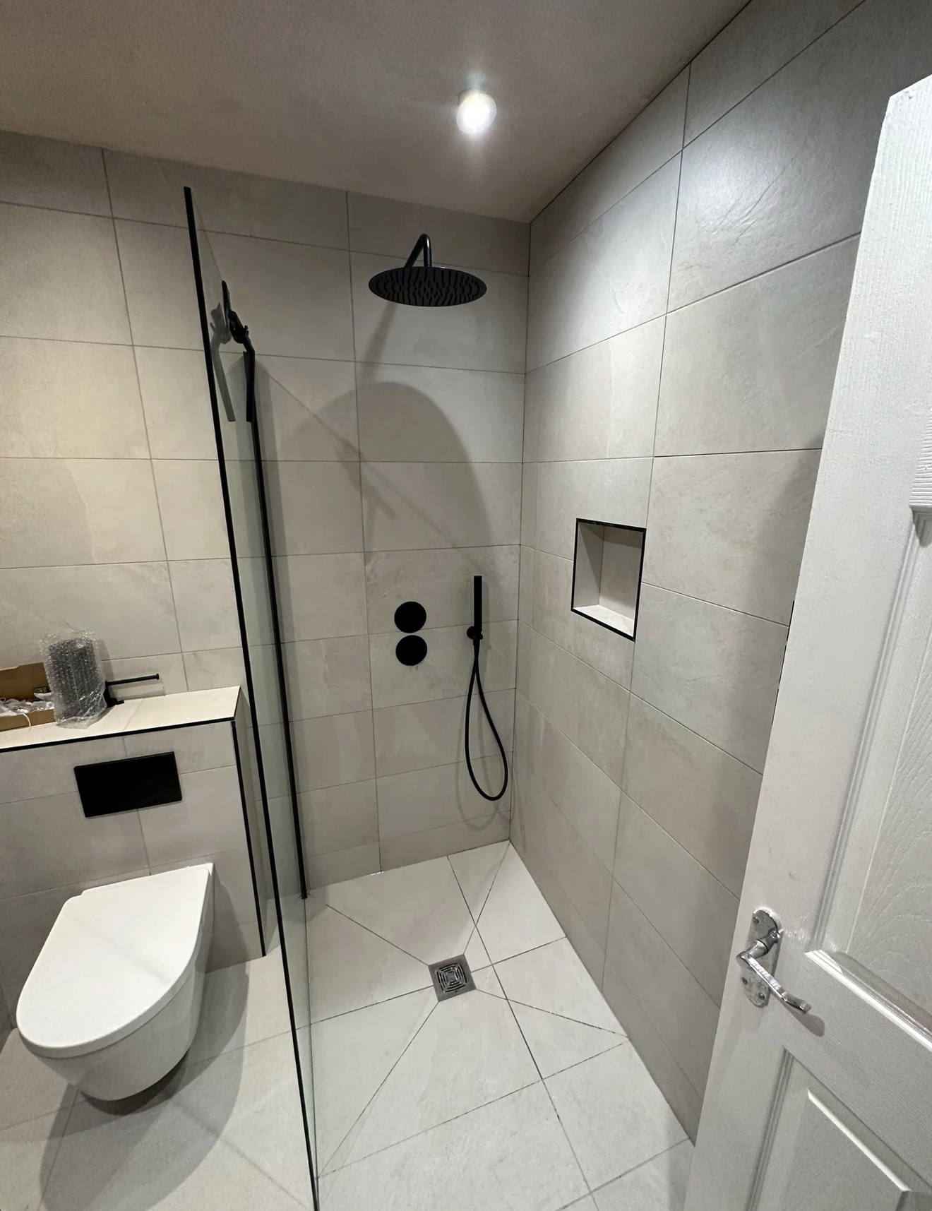 Compact wet room with matte black rainfall shower and framed glass screen — recent project Godalming
