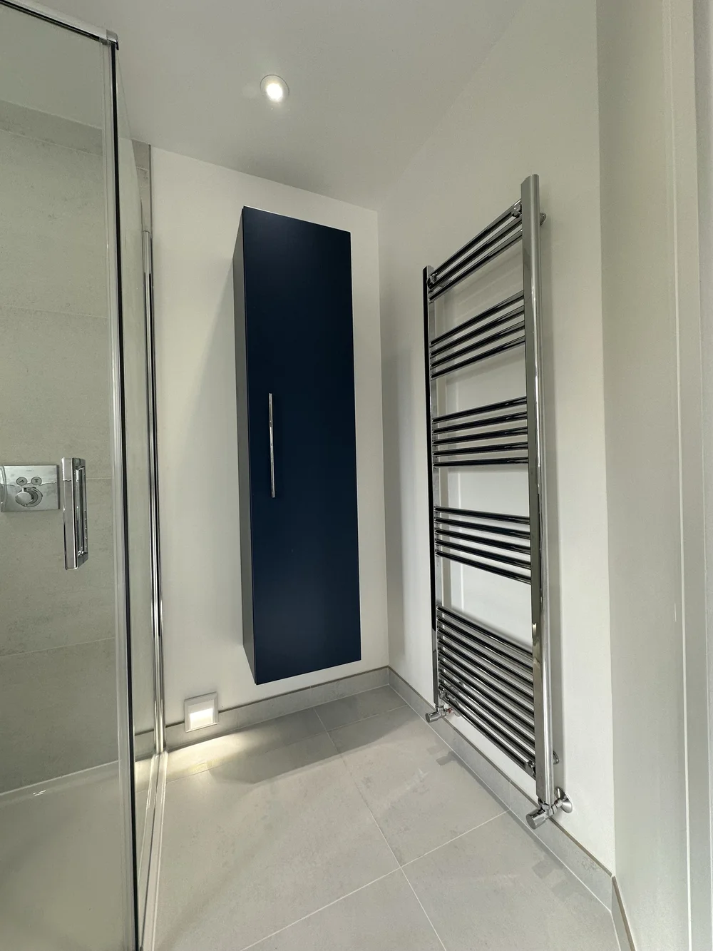 Detail of navy wall-hung storage cabinet with chrome ladder radiator — bathroom design Godalming