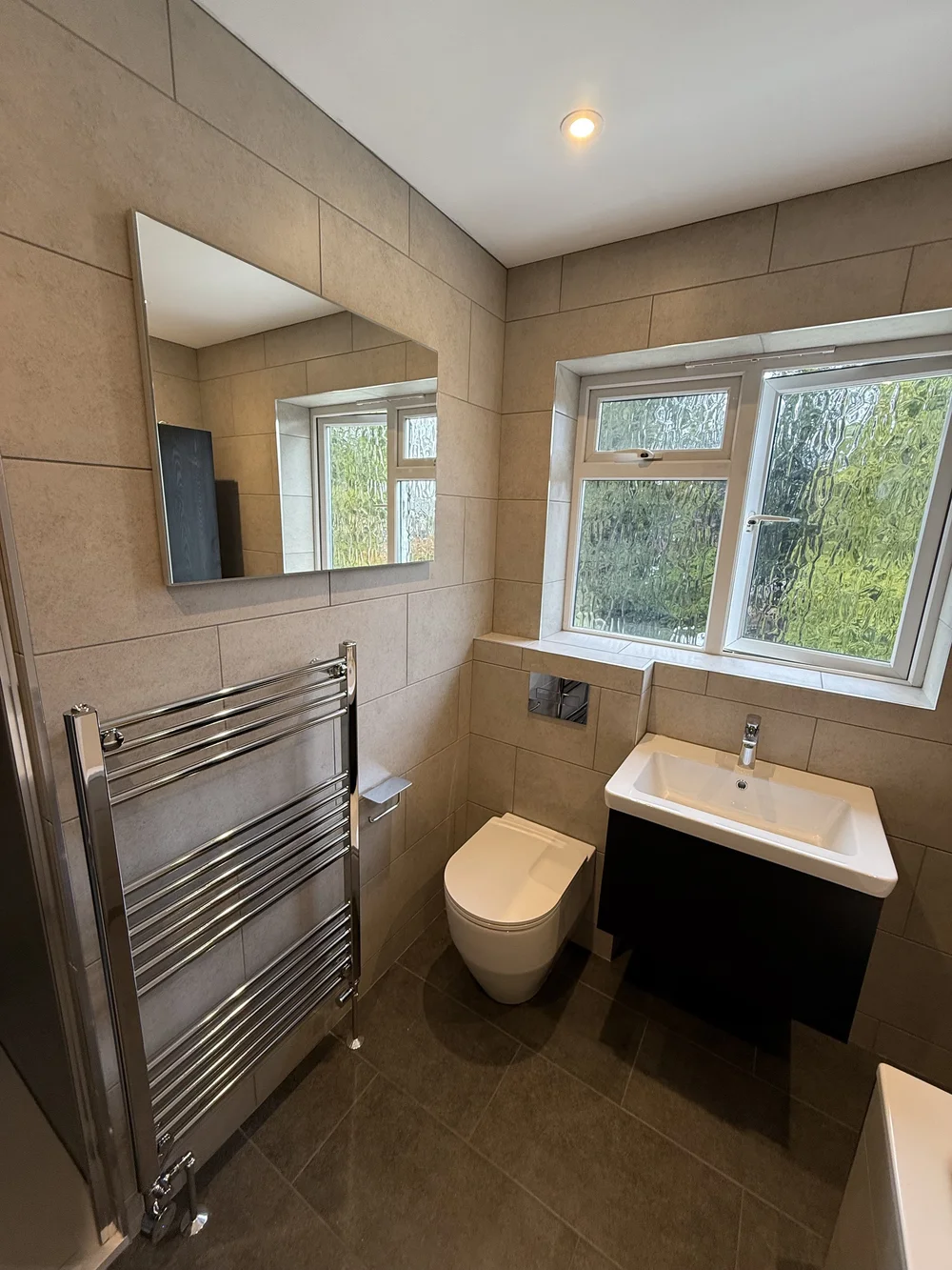 Beige-tiled bathroom with wall-hung black vanity and chrome heated rail — bathroom renovation Godalming