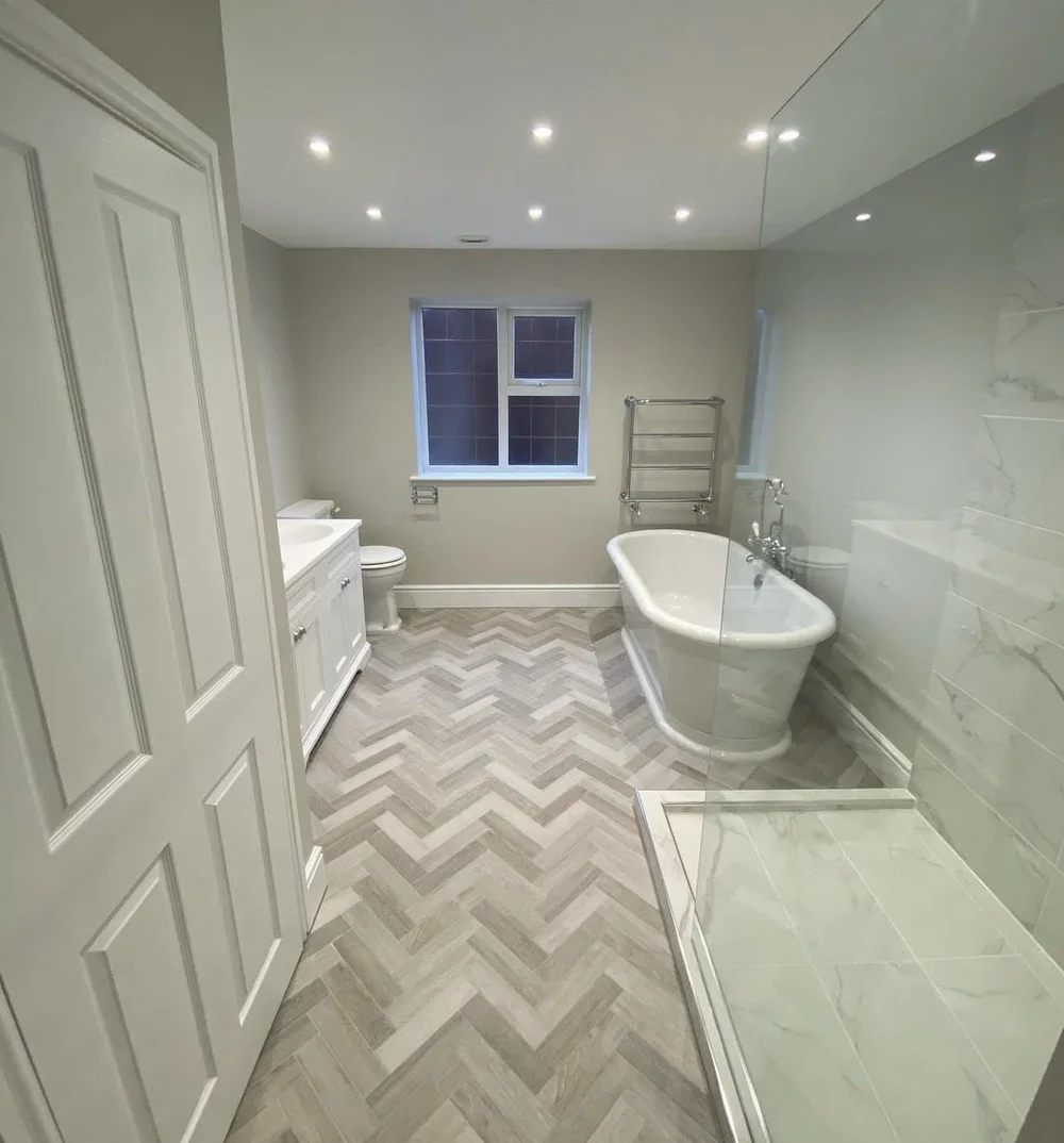 Traditional family bathroom with freestanding roll-top bath, herringbone floor and marble walk-in shower — bathroom installation Godalming