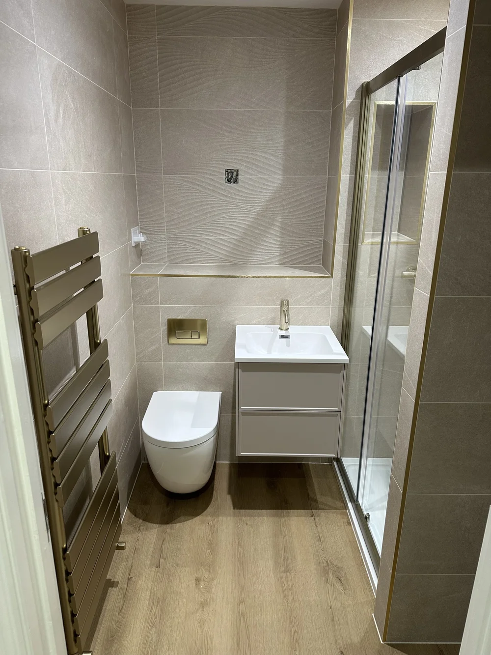 Textured stone shower room with brushed brass trim and designer towel rail — bathroom installation Godalming