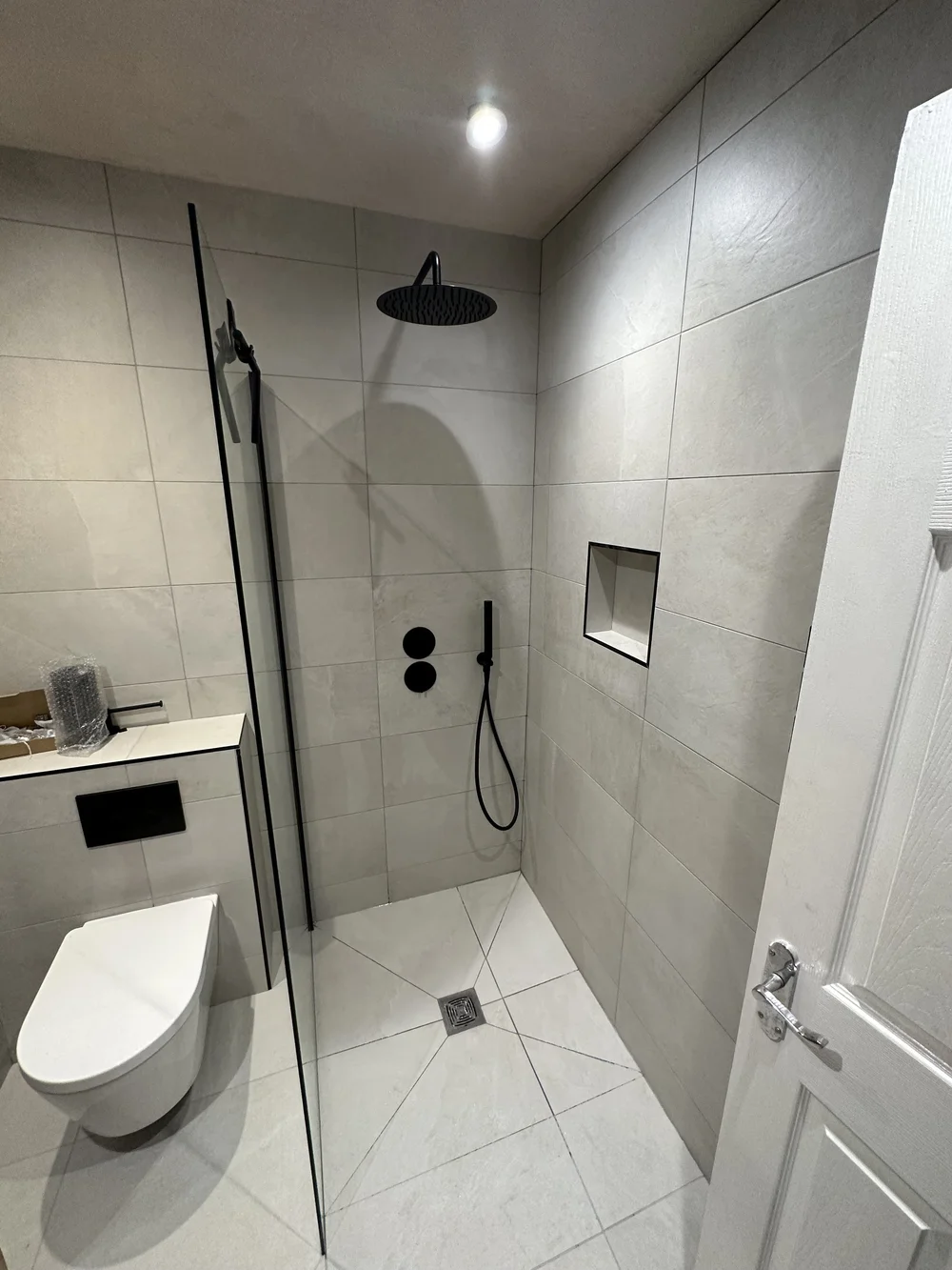 Stone-tiled walk-in shower with matte black rainfall head and recessed niche — wet room Godalming