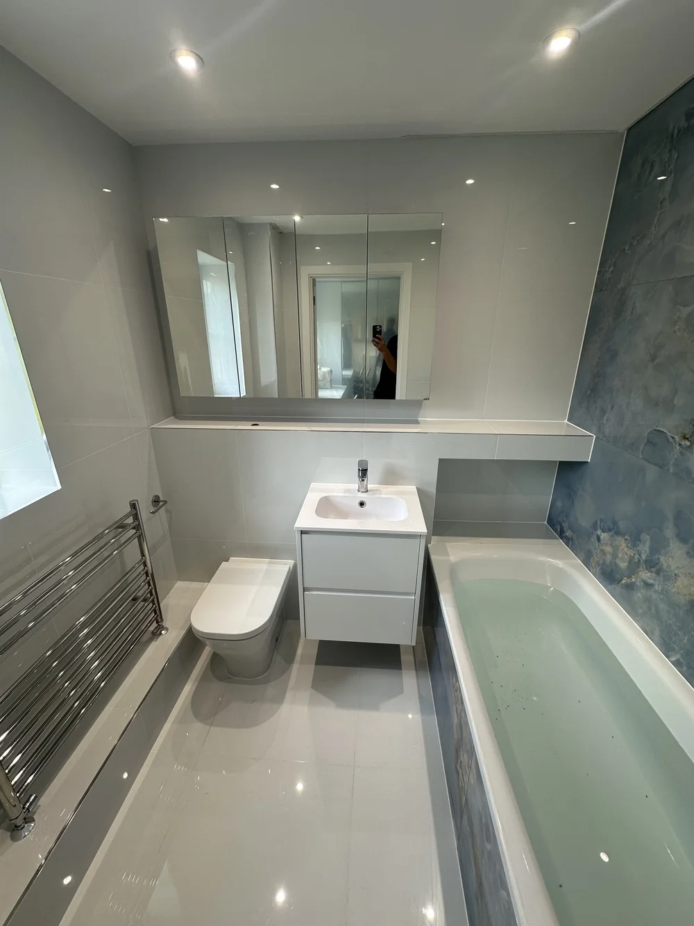 Bright family bathroom with mirrored cabinet, white vanity and blue onyx accent wall — bathroom renovation Godalming