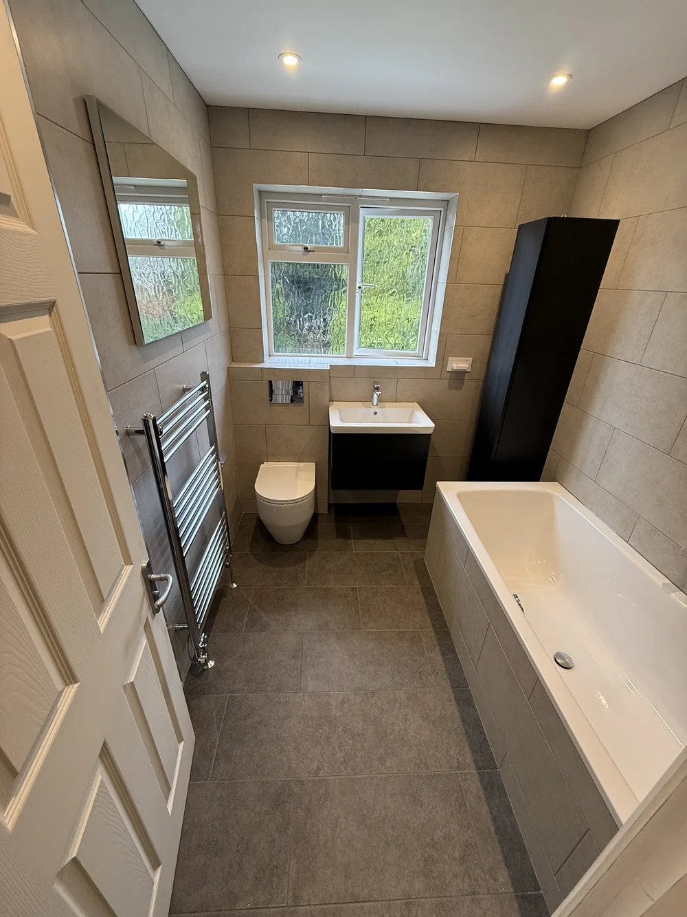 Compact family bathroom with black vanity, wall-hung WC and built-in bath — bathroom installation Godalming