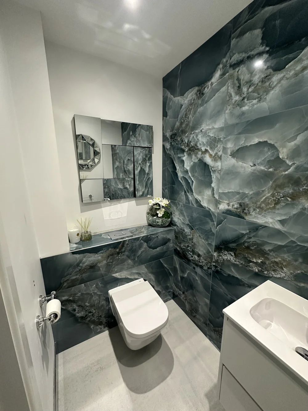 Bespoke cloakroom with full-height blue onyx feature wall and faceted mirror — bathroom design Godalming