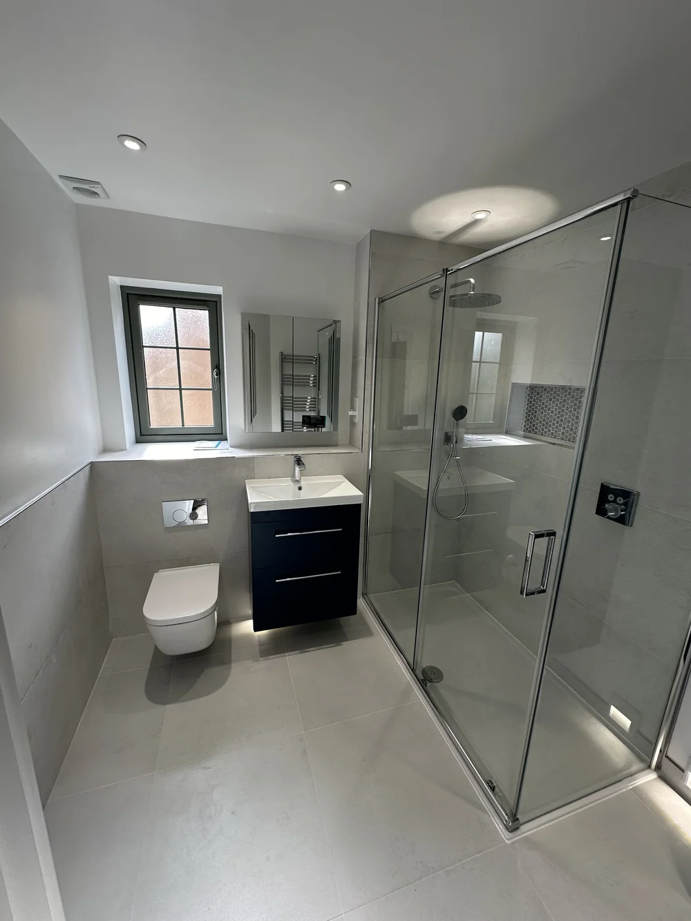 Fitted shower room with navy vanity, wall-hung WC and large glass shower enclosure — bathroom installation Godalming
