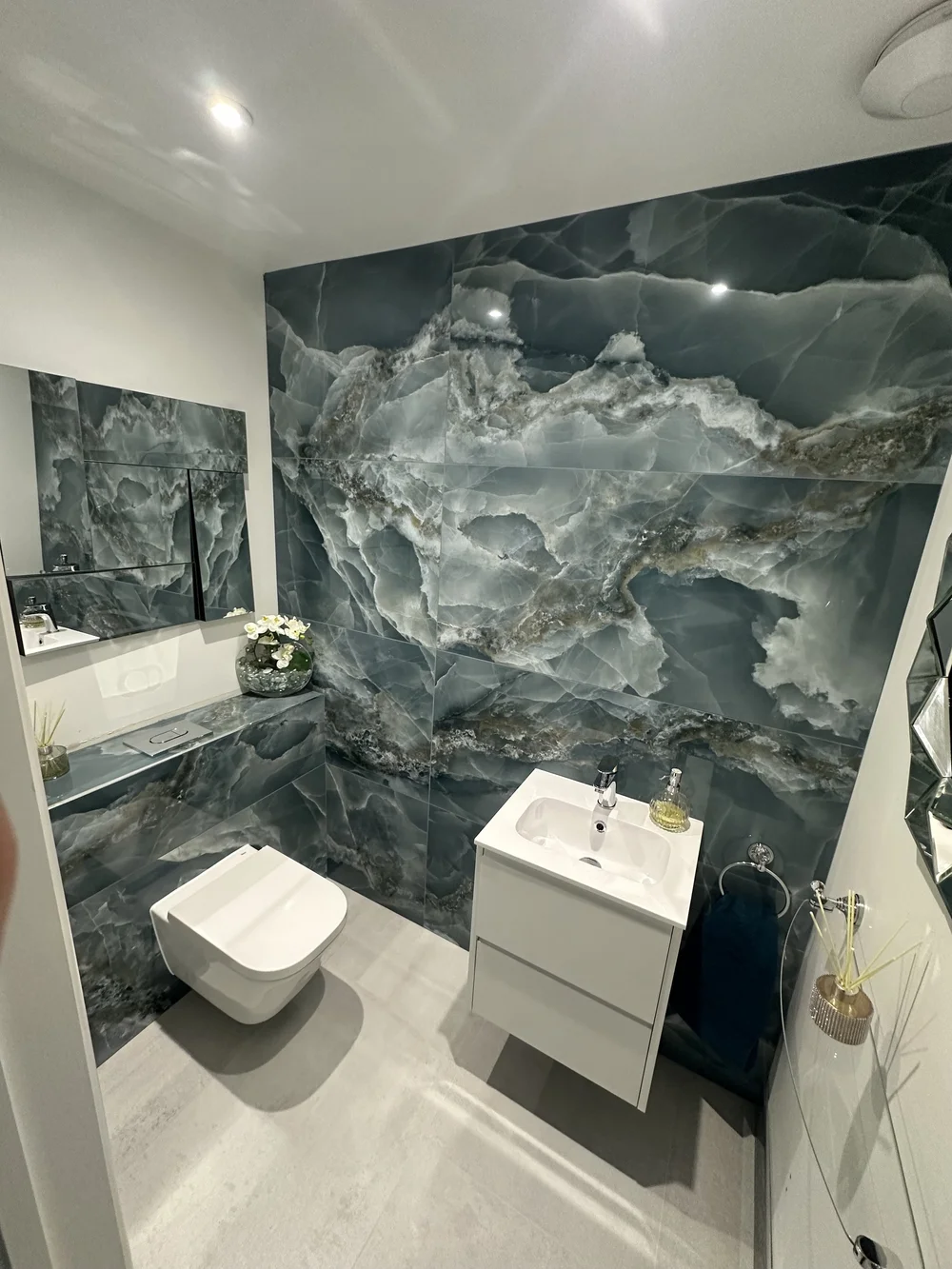 Cloakroom with blue onyx feature wall, wall-hung WC and floating white vanity — bathroom design Godalming