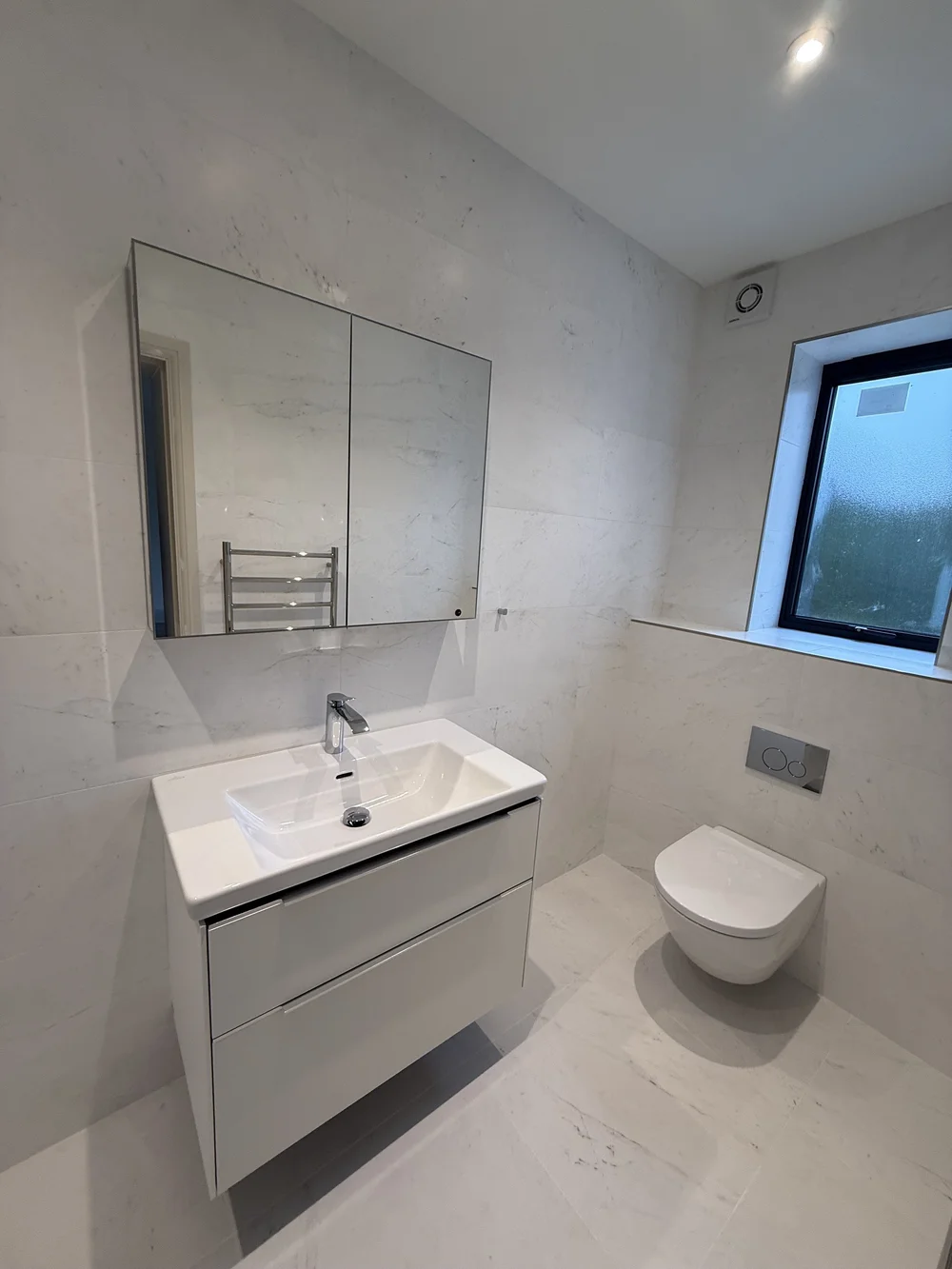 White marble family bathroom with wall-hung vanity and concealed cistern — Godalming