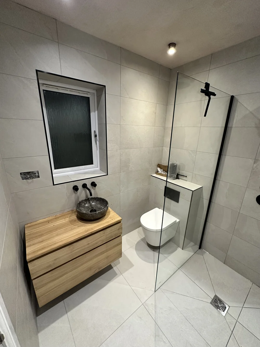 Wet room with oak floating vanity, stone basin and glass walk-in screen — wet room installation Godalming