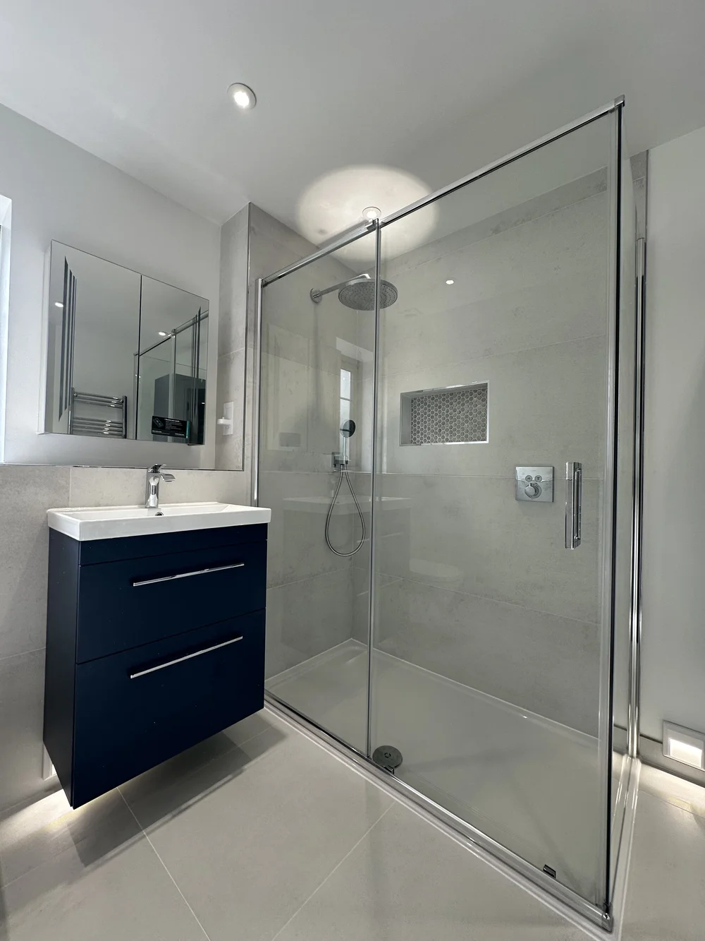 Modern ensuite with navy floating vanity, mirrored cabinet and sliding-door shower enclosure — bathroom installation Godalming
