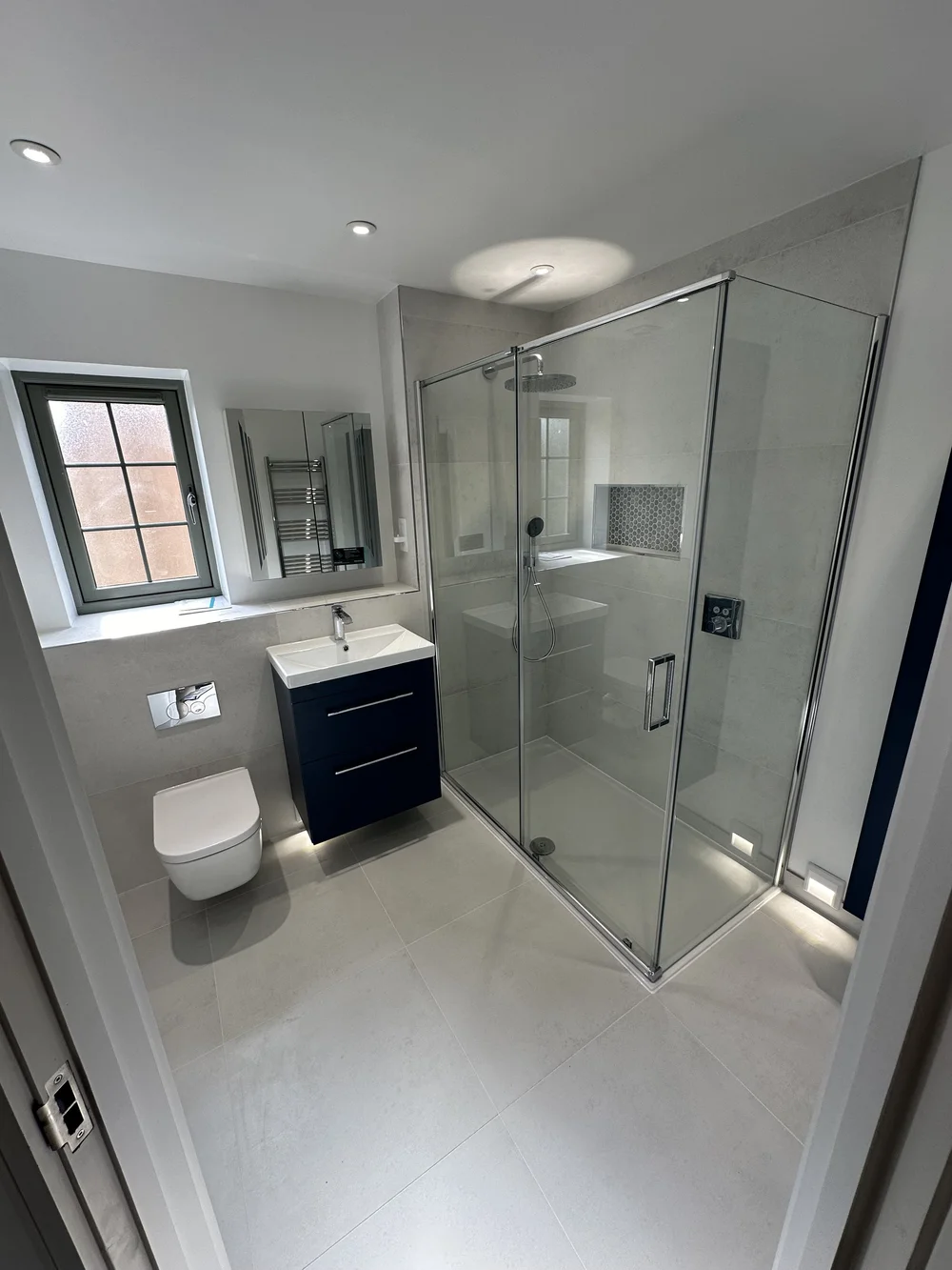 Fitted ensuite with navy vanity, wall-hung WC and corner shower enclosure — bathroom installation Godalming