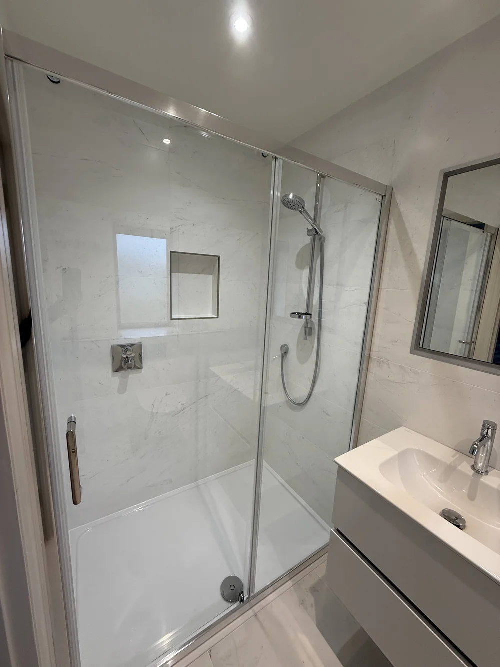Marble shower enclosure with sliding door and recessed niche — bathroom renovation Godalming