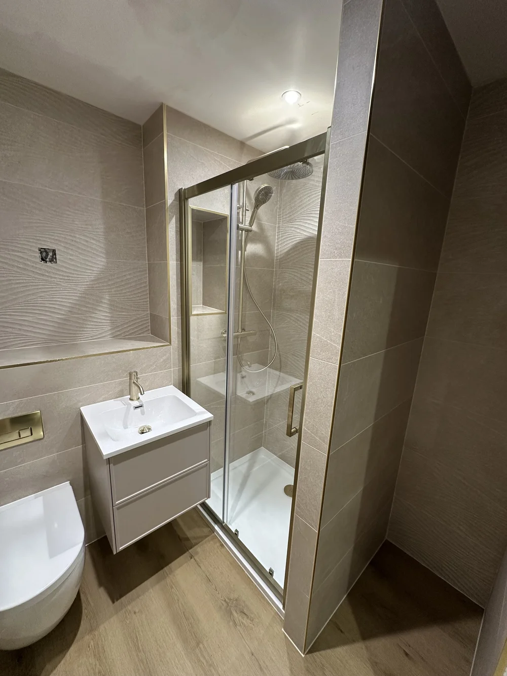 Wave-tiled shower room with brushed brass fittings and oak-effect floor — bathroom renovation Godalming