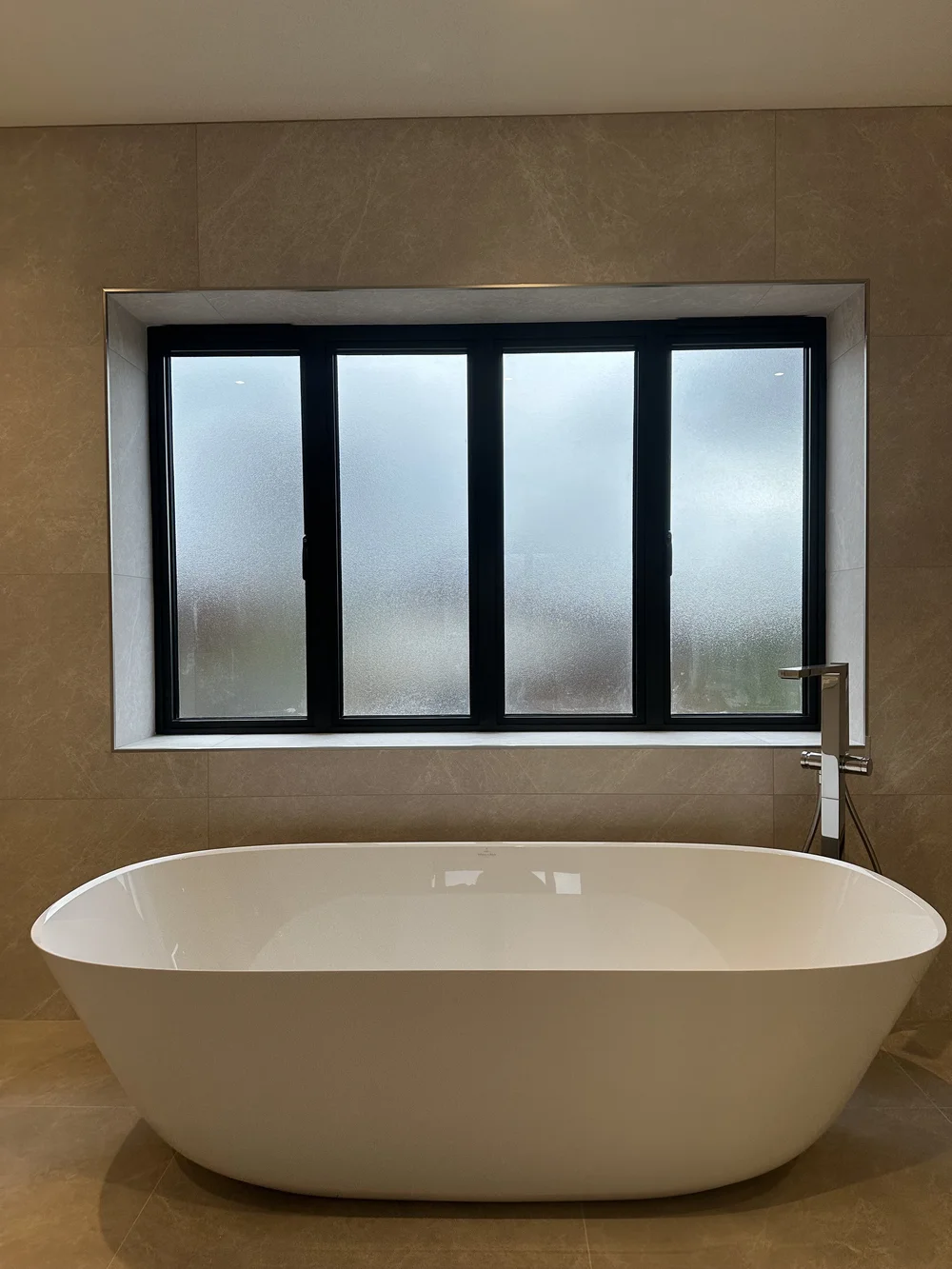 Freestanding stone-resin bath under crittall window in marble master bathroom — bathroom installation Godalming